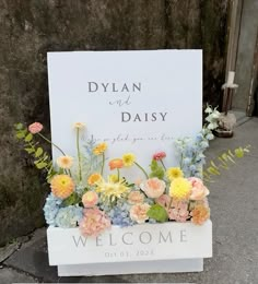 a welcome sign with flowers and greenery on it