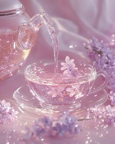 a glass tea cup filled with water next to purple flowers and a vase full of water