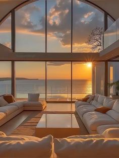 a living room filled with white furniture and large windows overlooking the ocean at sunset or sunrise