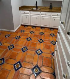 an orange and blue tile floor in a kitchen with white cabinets, counter tops and drawers