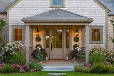 the front door of a house with two wreaths on it's windows and flowers