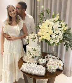 a man and woman standing next to a table filled with cakes, cupcakes and flowers