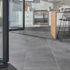 a kitchen with grey tile flooring and white cabinets, an island table and bar stools