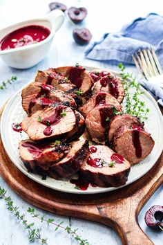 sliced pork with cranberry sauce on a white plate next to a wooden spoon