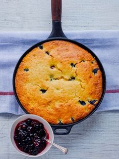 a blueberry cobbler in a cast iron skillet next to a bowl of jam