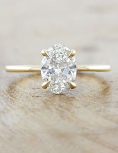 an oval cut diamond sits on top of a wooden surface, with the center stone in yellow gold