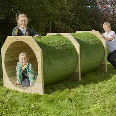 two children and an adult playing in a fake grass tunnel