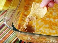 a person dipping a tortilla chip into a casserole dish with cheese