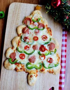 a christmas tree shaped pizza on a cutting board with pepperoni and jalapenos