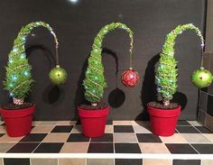 three potted plants with christmas decorations on them sitting on a tiled countertop in front of a black wall