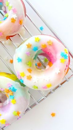 three donuts with icing and sprinkles are on a cooling rack