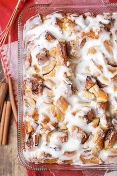 a glass dish filled with cinnamon rolls covered in white icing next to cinnamon sticks