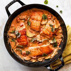 a skillet filled with salmon and vegetables on top of a white table next to a yellow towel