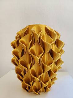 a yellow vase sitting on top of a white table covered in ruffled paper pieces