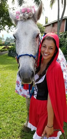 a woman in a red cape standing next to a horse