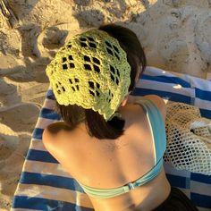 a woman laying on top of a blue and white towel wearing a green crocheted hat