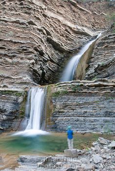 a man is standing at the base of a waterfall and looking up into the water