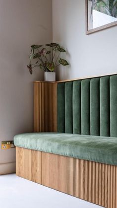 a wooden bench with green velvet upholster and plant in vase on the wall