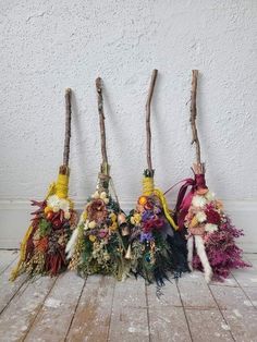 four brooms are lined up on the floor with flowers and feathers attached to them