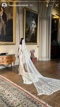 a woman in a white wedding dress standing next to a painting on the wall and wearing a long veil