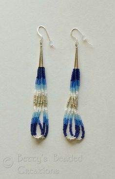 blue and white beaded earrings hanging from hooks on a white surface with the word bead creations written below it