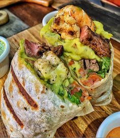 a wrap filled with meat and vegetables on top of a wooden cutting board