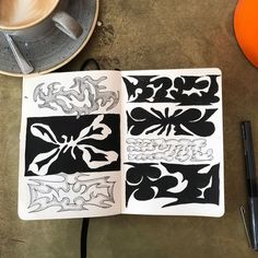 an open notebook with designs on it next to a cup of coffee and a pen