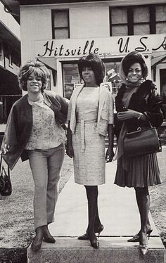 three women are standing on the sidewalk in front of a building with a sign that says kitssville u s a