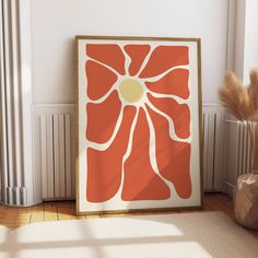 an orange and white flower is on the floor next to a vase with some dry grass in it