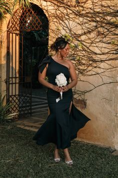 a woman standing in front of a building wearing a black dress and holding a bouquet