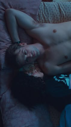 a shirtless man and woman laying on a bed next to each other in the dark