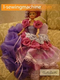 a doll is sitting on a couch wearing a purple and pink dress with roses in the skirt