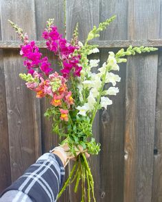 a person holding a bouquet of flowers in front of a wooden fence with wood slats