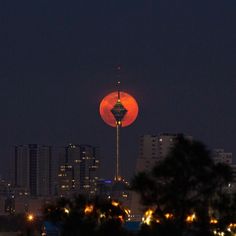 the full moon is seen over a city at night with tall buildings in the background