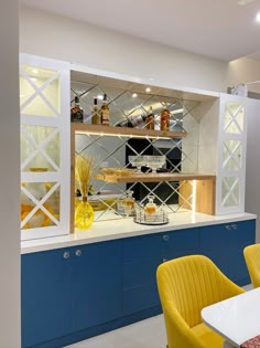 a kitchen with blue cabinets and yellow chairs in front of the counter top, along with shelves that have bottles on them