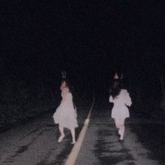 two people in white dresses are walking down the road at night with their hands up