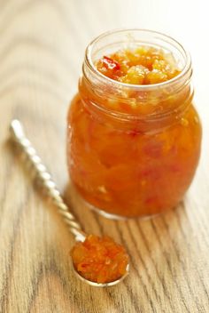 a glass jar filled with jelly sitting on top of a table next to a spoon