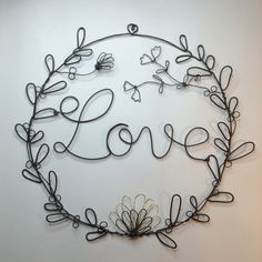 a metal wall hanging with the word love written in it's center surrounded by leaves and flowers