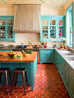 a kitchen with blue cabinets and wooden counter tops, red tile flooring and an island in the middle