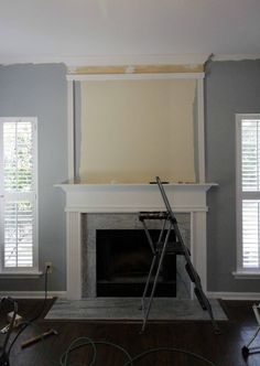 an empty living room with a fireplace in the middle and paint being applied on the walls