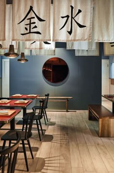 a restaurant with chinese writing hanging from the ceiling and wooden tables in front of them