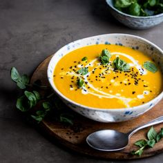 a bowl of carrot soup on a wooden board with two bowls of salad in the background