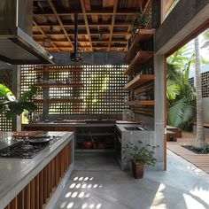 an outdoor kitchen with wooden shelves and plants on the counter top, surrounded by palm trees