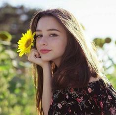 a woman holding a sunflower in her hand and looking at the camera with a smile on her face