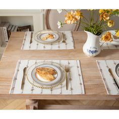 the table is set with plates, silverware and yellow flowers in a white vase