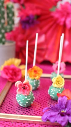 cake pops decorated with flowers and candles on a pink tablecloth in front of a potted plant