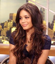 a beautiful young lady sitting down in front of a tv screen with the city skyline behind her