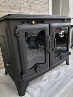 an old fashioned black stove sitting on top of a white sheet covered floor next to a brick wall