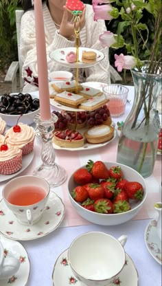 a table topped with plates and cups filled with desserts next to a vase full of strawberries