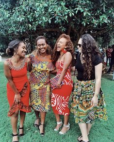 three women standing next to each other in front of a tree and grass covered field